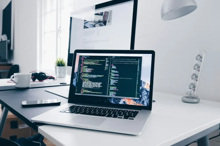 Máy tính hiển thị mã nguồn và giao diện website trên bàn làm việc